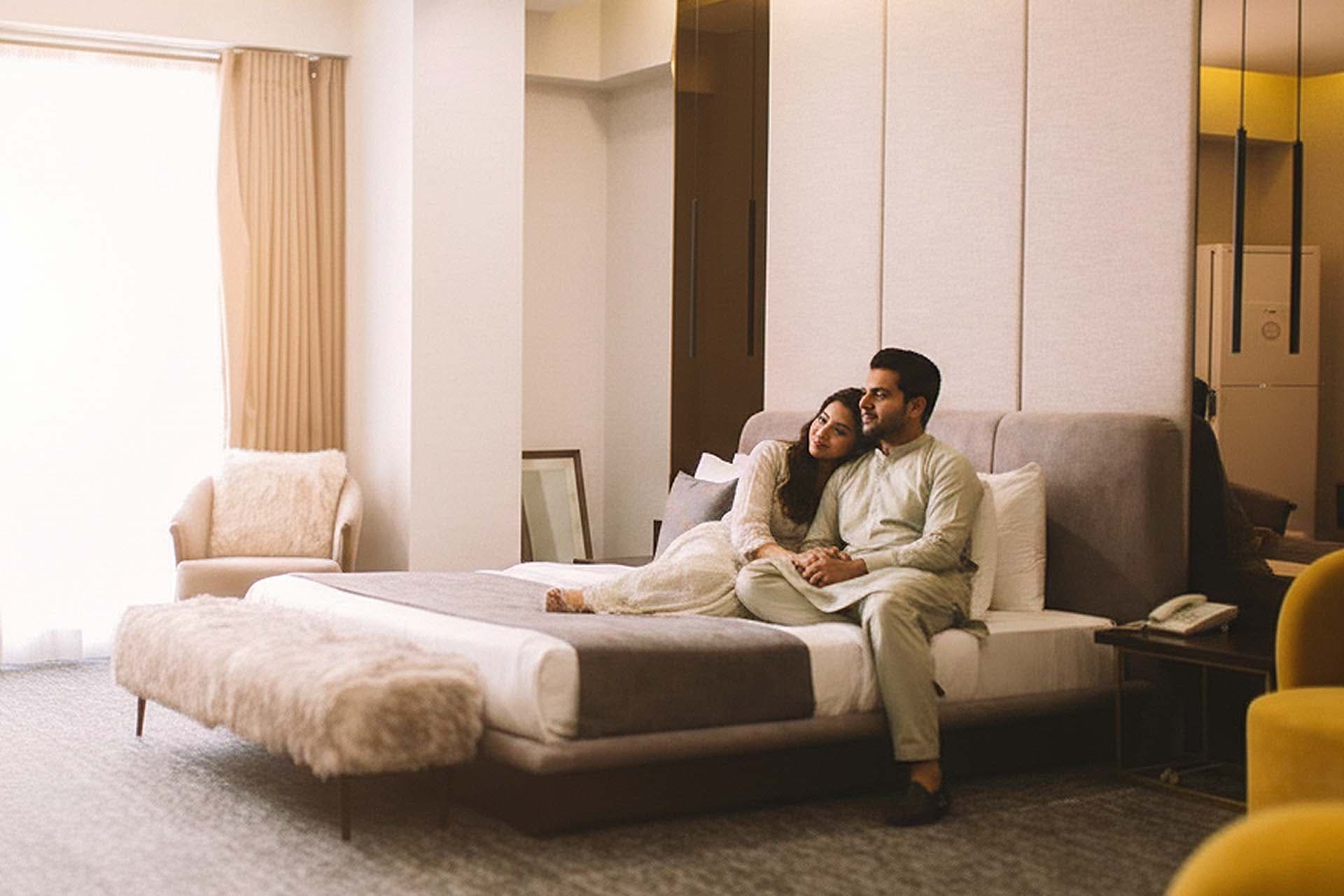 Couple relaxing on a cozy hotel bed at LEORK Hotels Rawalpindi, watching TV and enjoying a romantic stay