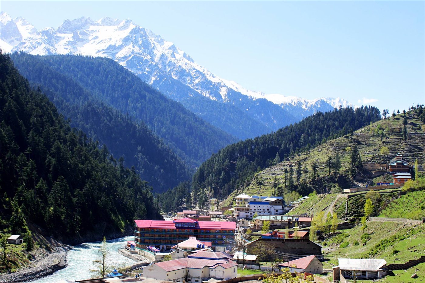 Swat River flowing past Kalam town with pine forests and snow peaks behind