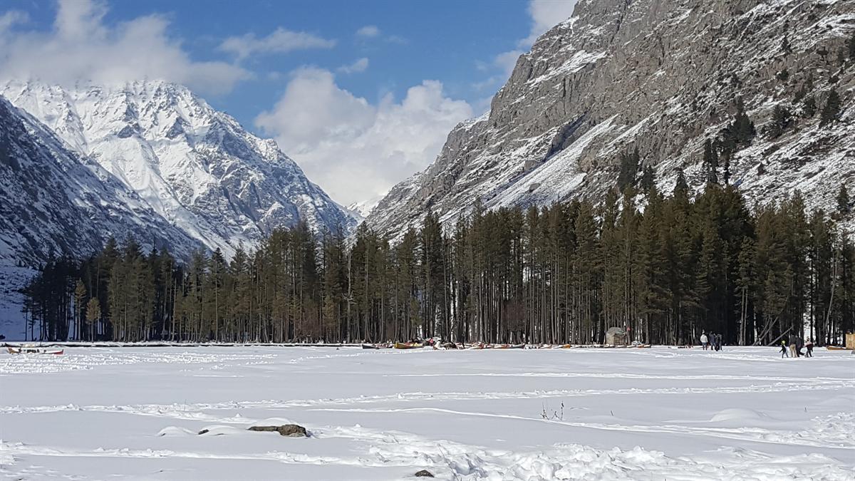 Mahodand Lake frozen and covered in snow in winter, with boats parked by the tree line