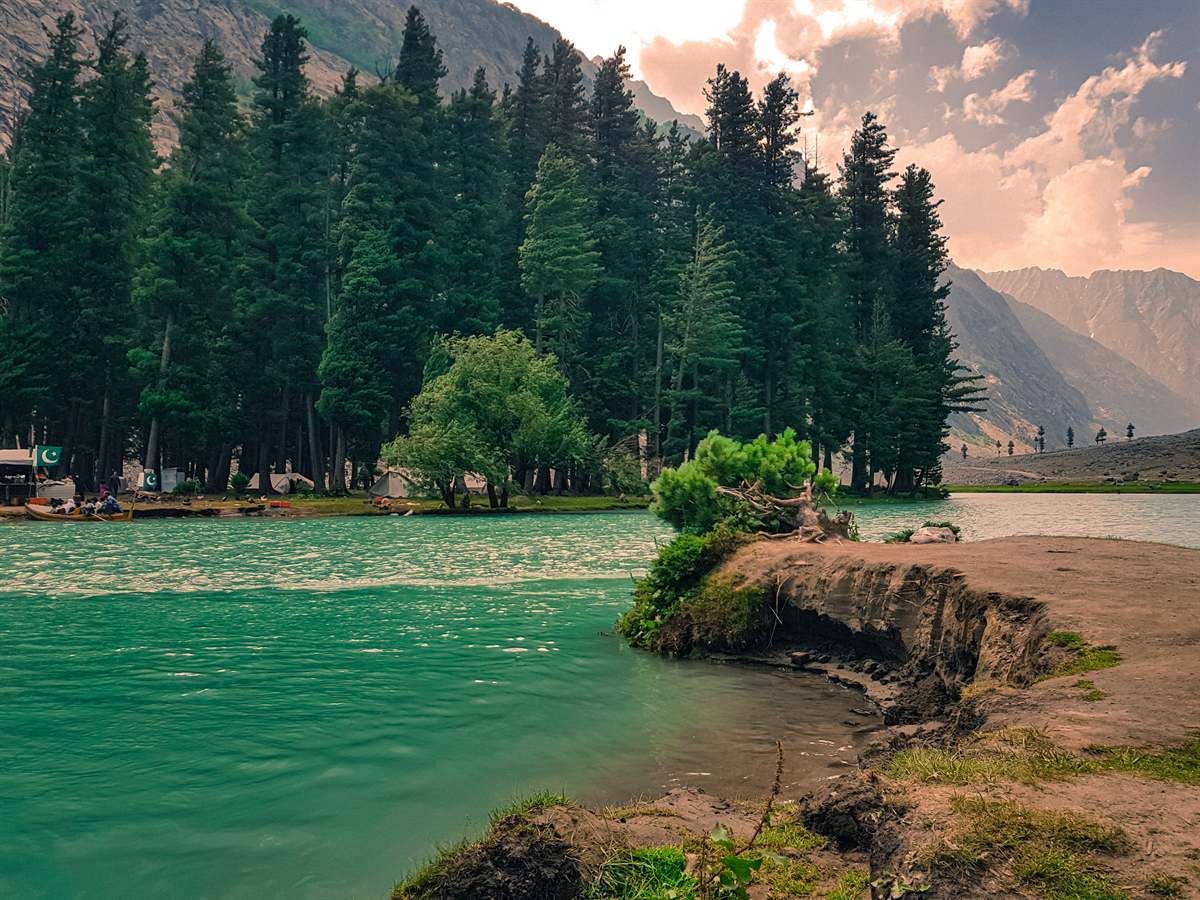Deep turquoise water of Saifullah Lake with pine forest, tents and cliffs beyond Mahodand