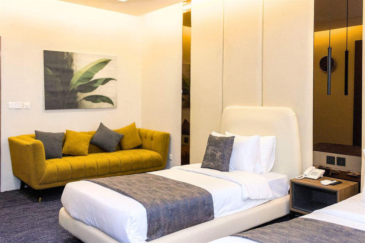 Family Room at LEORK Hotels Rawalpindi with two beds and a mustard sofa seating area