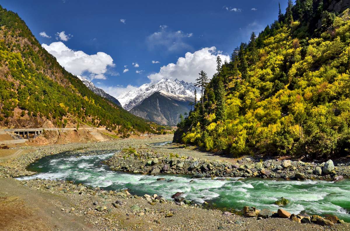 The Swat River curving below forested slopes and a snow-capped peak on the road to Kalam.