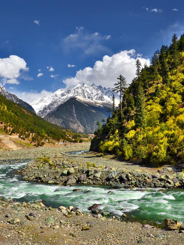 The Swat River curving below forested slopes and a snow-capped peak on the road to Kalam.