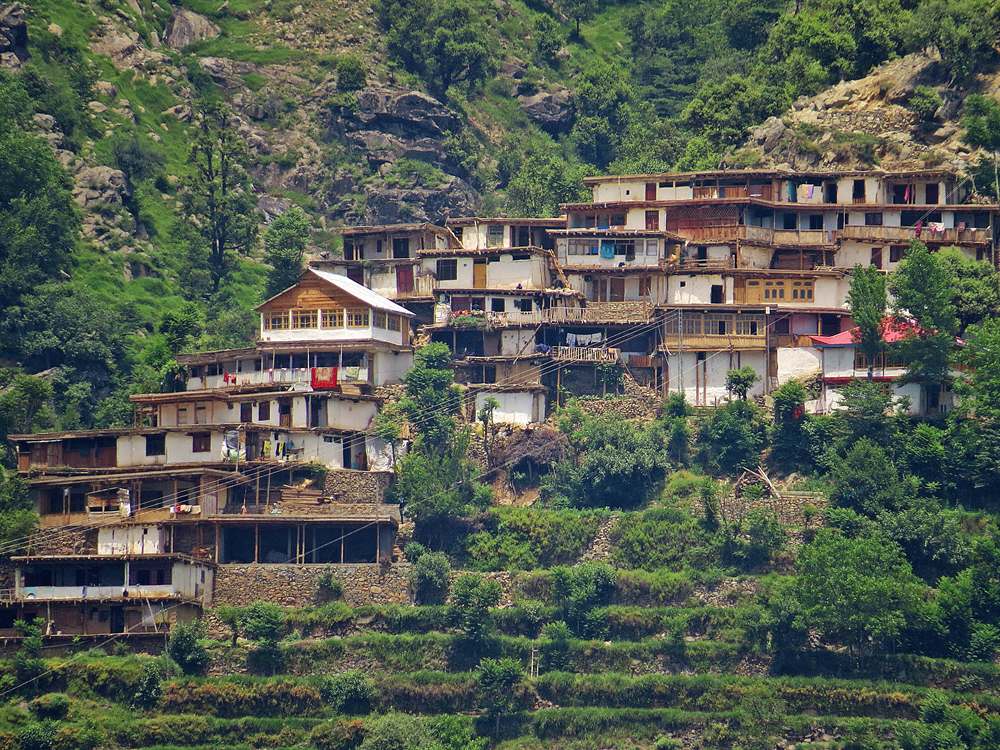 Traditional wooden houses stacked on a green hillside in Madyan, Swat Valley