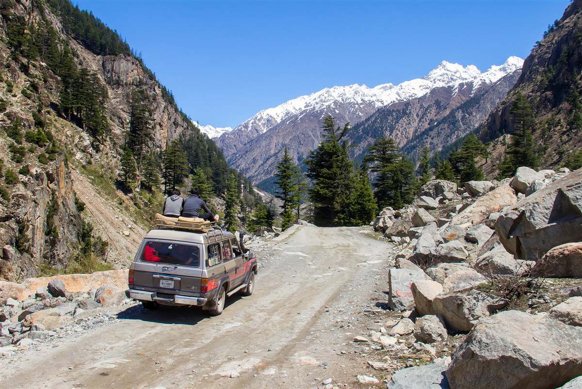 Jeep carrying passengers up an unpaved mountain track near Kalam with snow peaks ahead