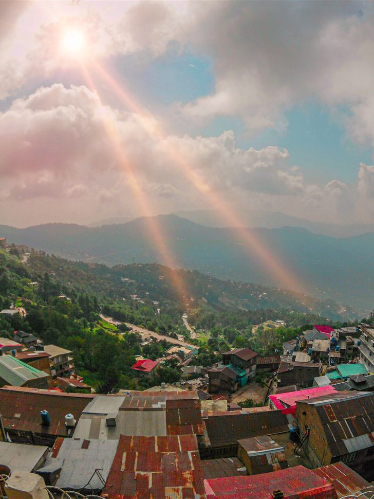 View over Murree's rooftops and forested hills with sun rays breaking through the clouds.