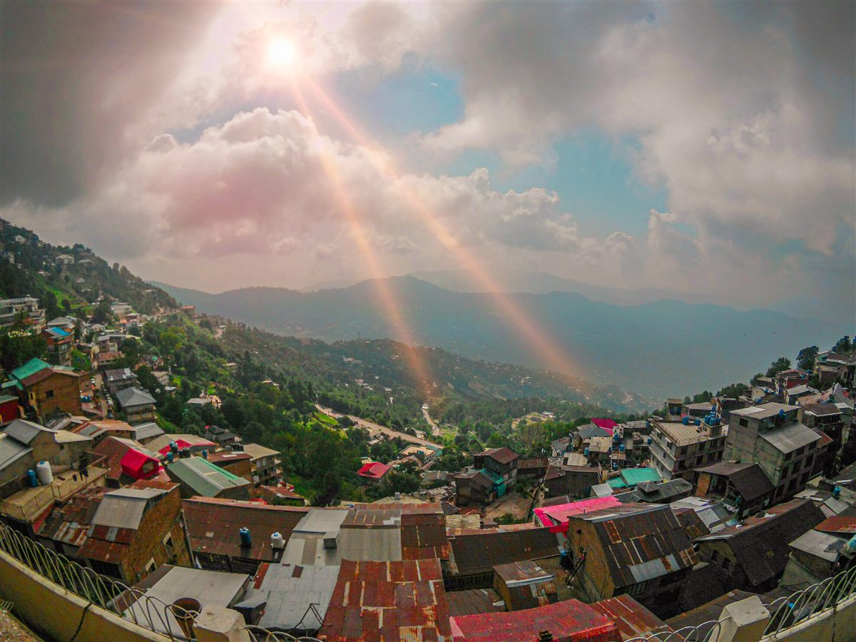 View over Murree's rooftops and forested hills with sun rays breaking through the clouds.