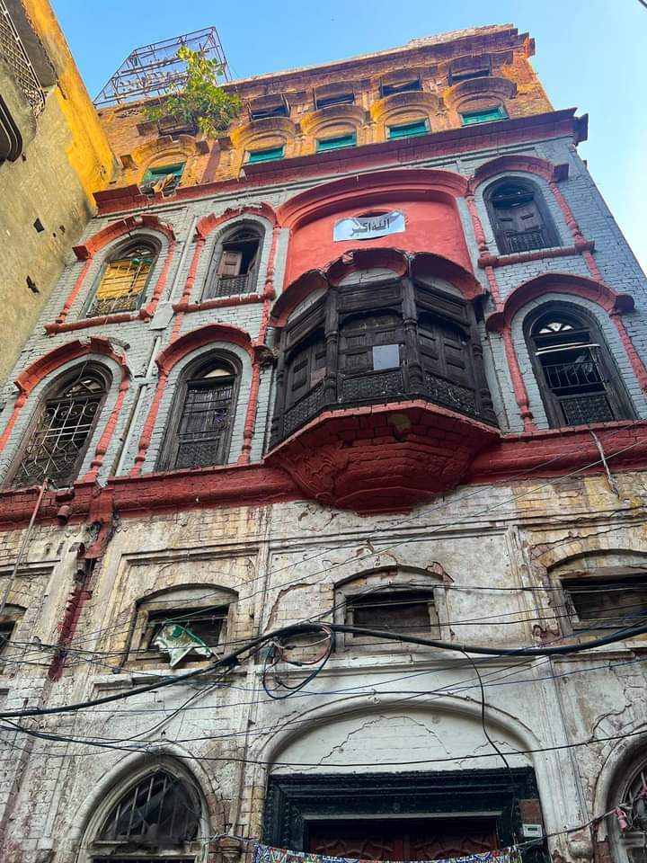 Weathered heritage building with a wooden jharoka balcony above the shops of Raja Bazaar, Rawalpindi