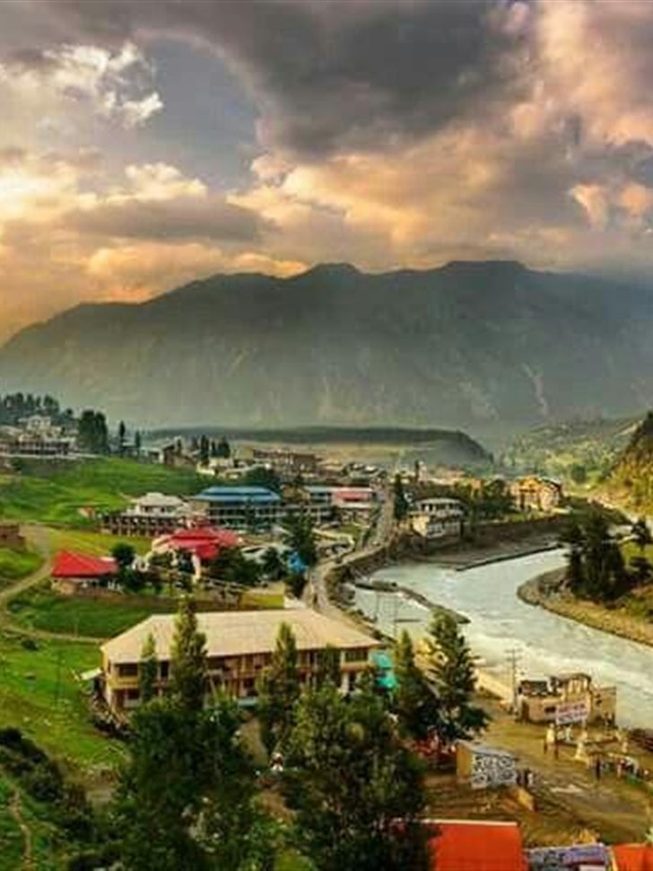 Kalam town and the Swat River at golden hour, ringed by green hillsides and mountains.