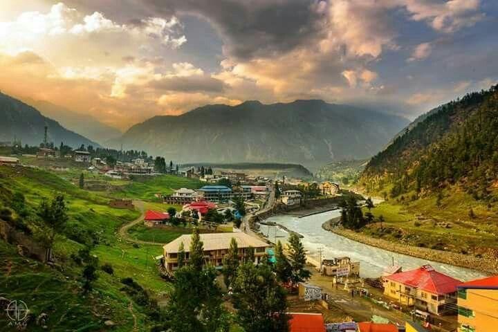 Kalam town and the Swat River at golden hour, ringed by green hillsides and mountains.