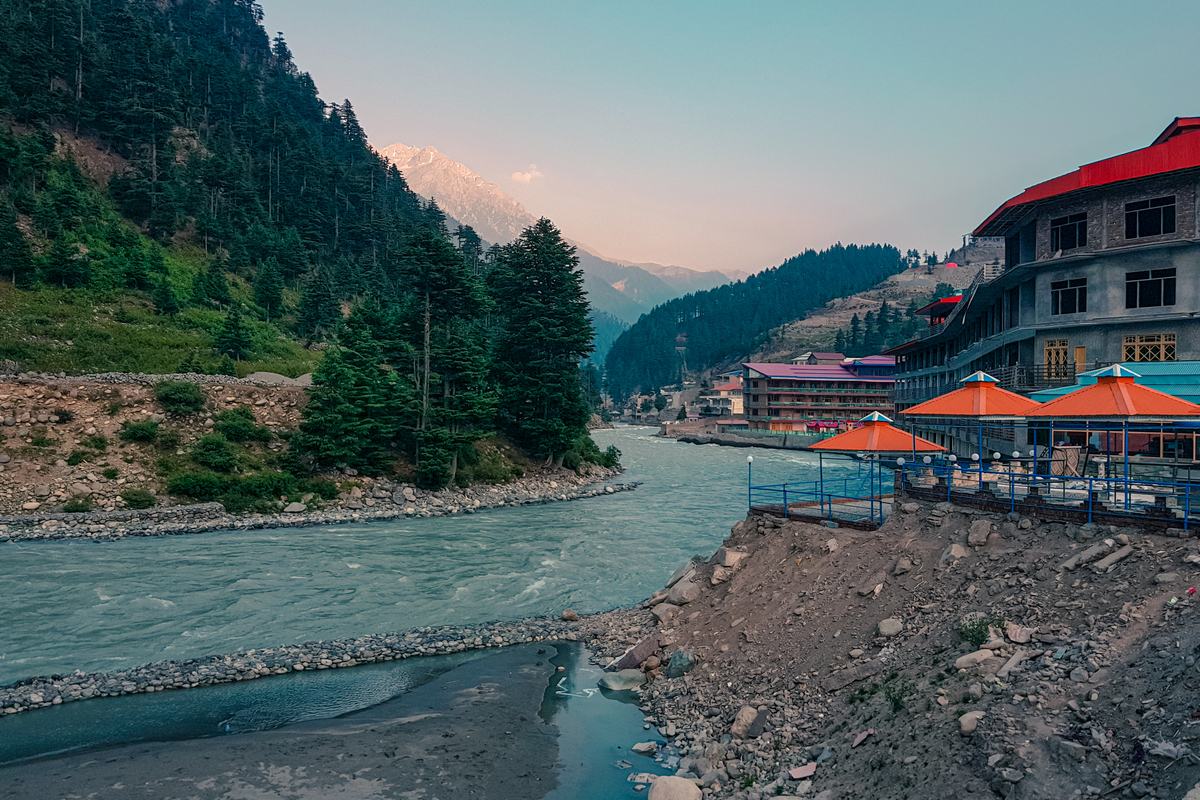 Riverside hotels with orange umbrellas along the Swat River in Kalam at dusk, with a snow peak behind.