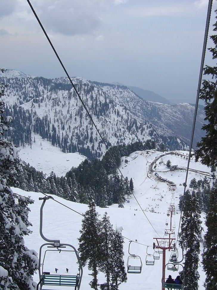 View from the chairlift at Malam Jabba down through snow-covered pines to a busy ski slope.