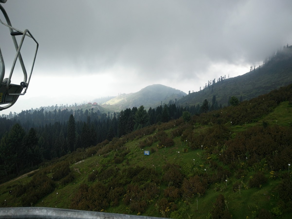 View from a Malam Jabba chairlift seat over green summer meadows and pine forest