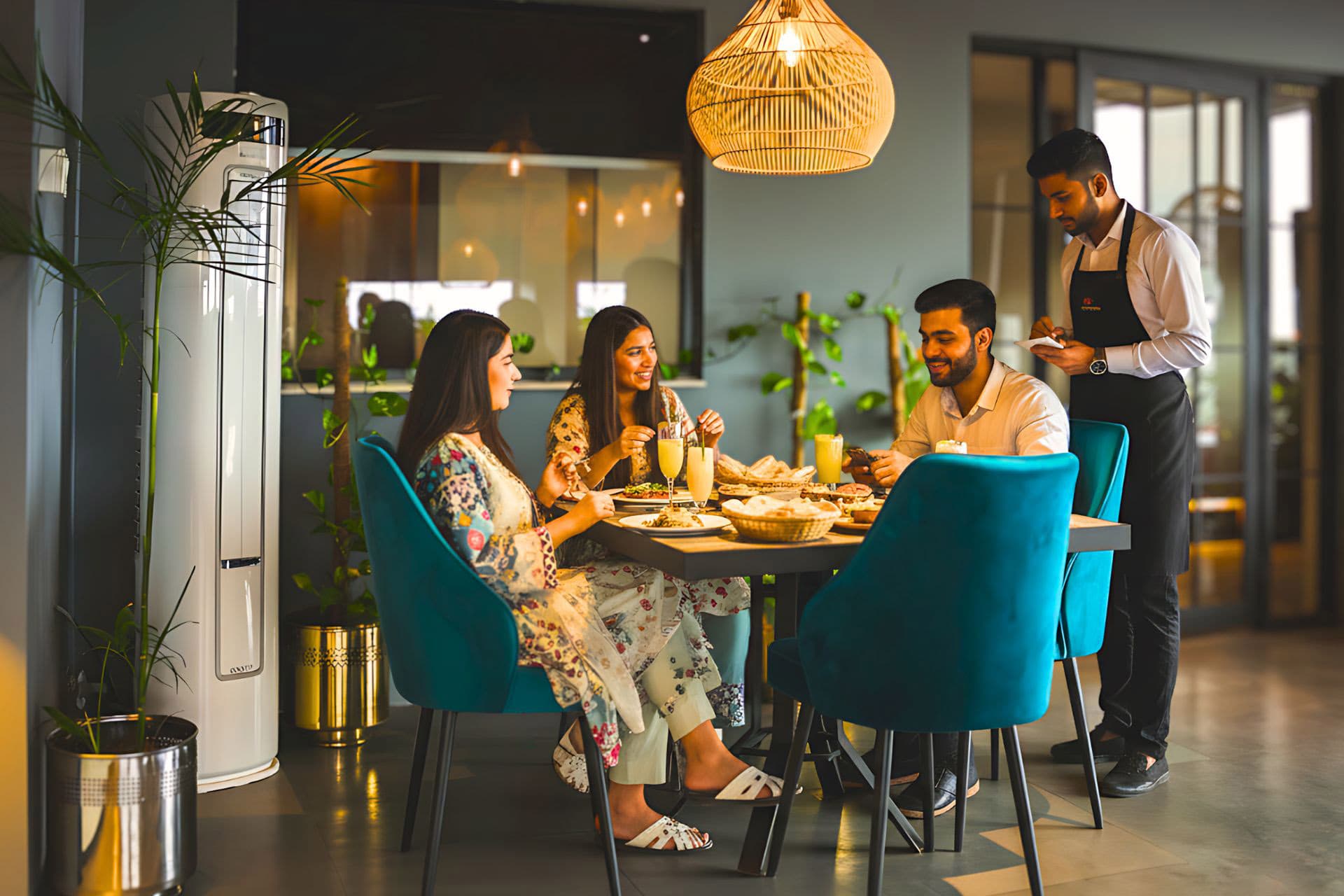 Little Tree Café with two women and one man enjoying cocktails and burgers, fancy lights, plants, chairs, table, and vibrant atmosphere with large windows at LEORK Hotels Rawalpindi Islamabad