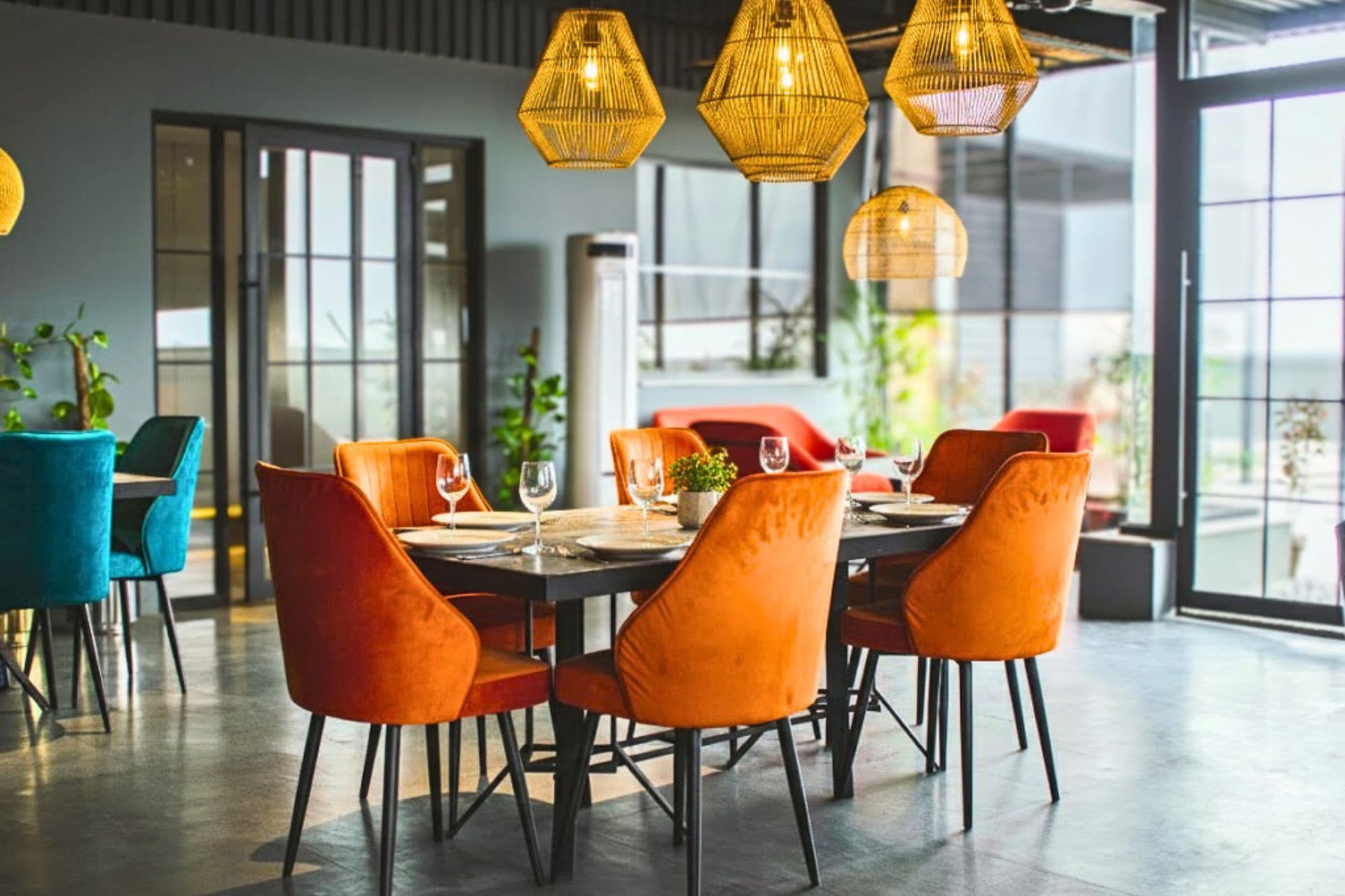 Little Tree Café terrace view with six-seater table, chic orange chairs, set table, warm lights, plants, and inviting ambiance with large windows at LEORK Hotels Rawalpindi Islamabad