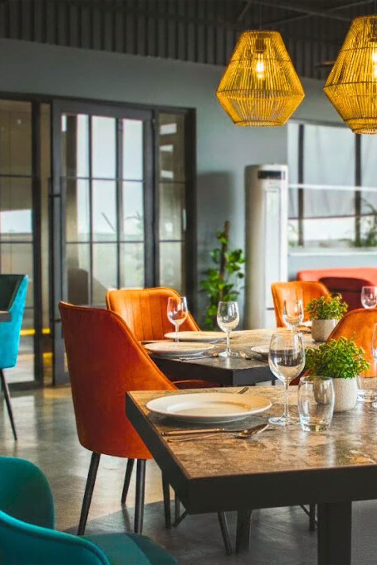 Little Tree Café mobile full view with orange and teal chairs, set tables, food, vibrant atmosphere, plants, and large windows at LEORK Hotels Rawalpindi Islamabad