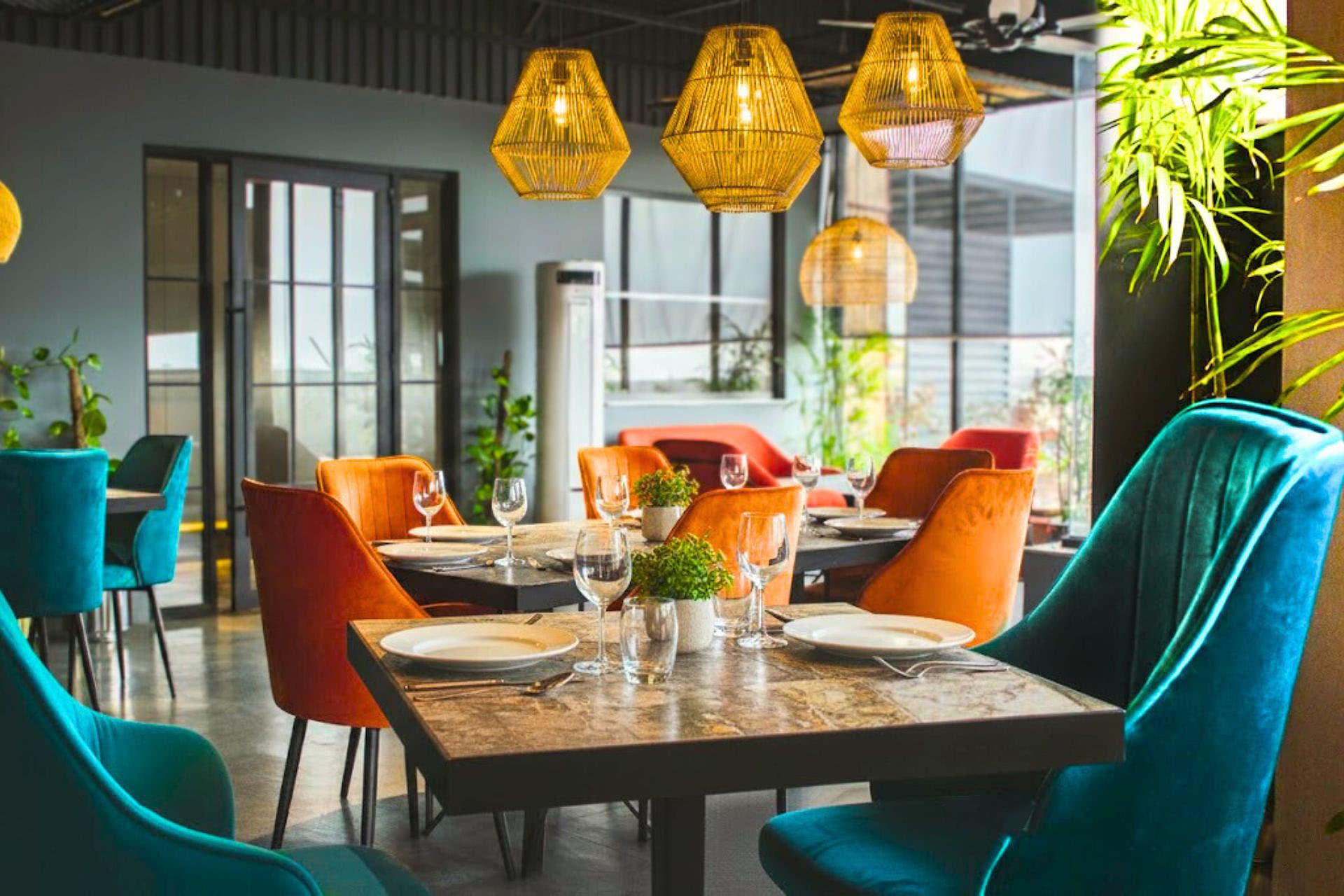 Little Tree Café full view with orange and teal chairs, set tables, delicious food, lively ambiance, plants, and large windows at LEORK Hotels Rawalpindi Islamabad