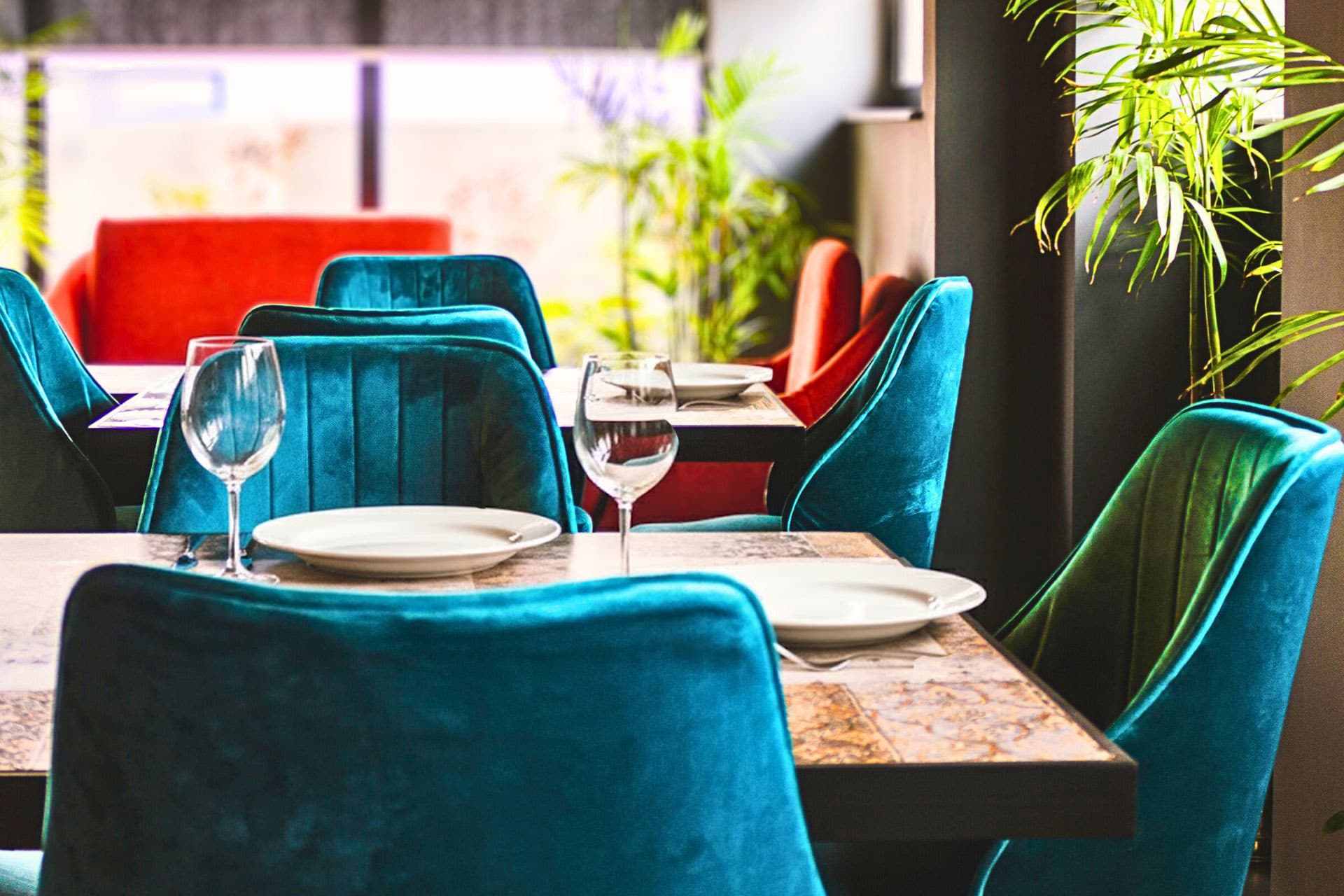 Little Tree Café close-up of teal chairs, chair details, plants, vibrant ambience, warm lighting, and atmosphere with large windows at LEORK Hotels Rawalpindi Islamabad