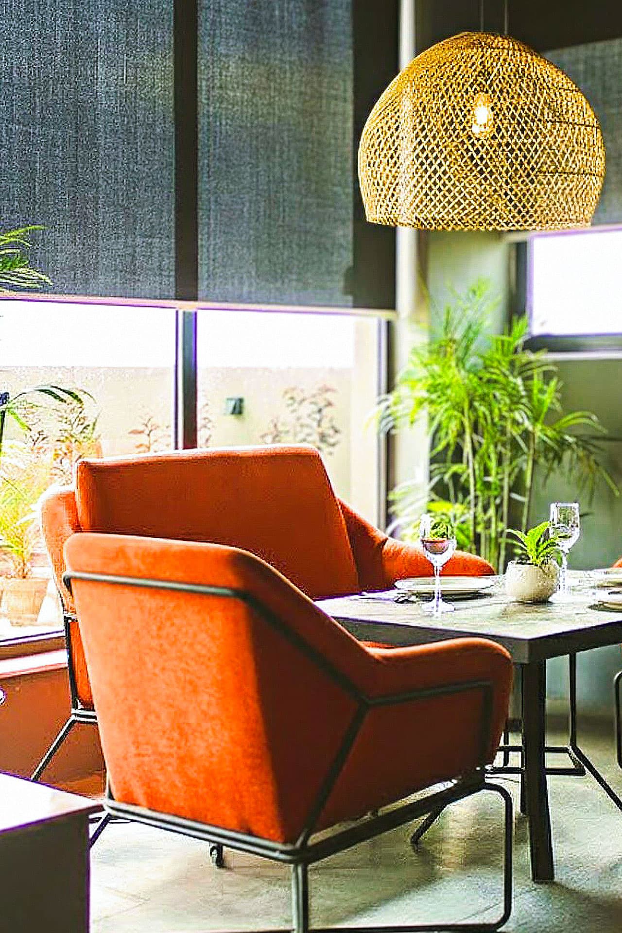 Little Tree Café mobile view with red chairs, coffee table, plants, outside view, and cozy atmosphere at LEORK Hotels Rawalpindi Islamabad