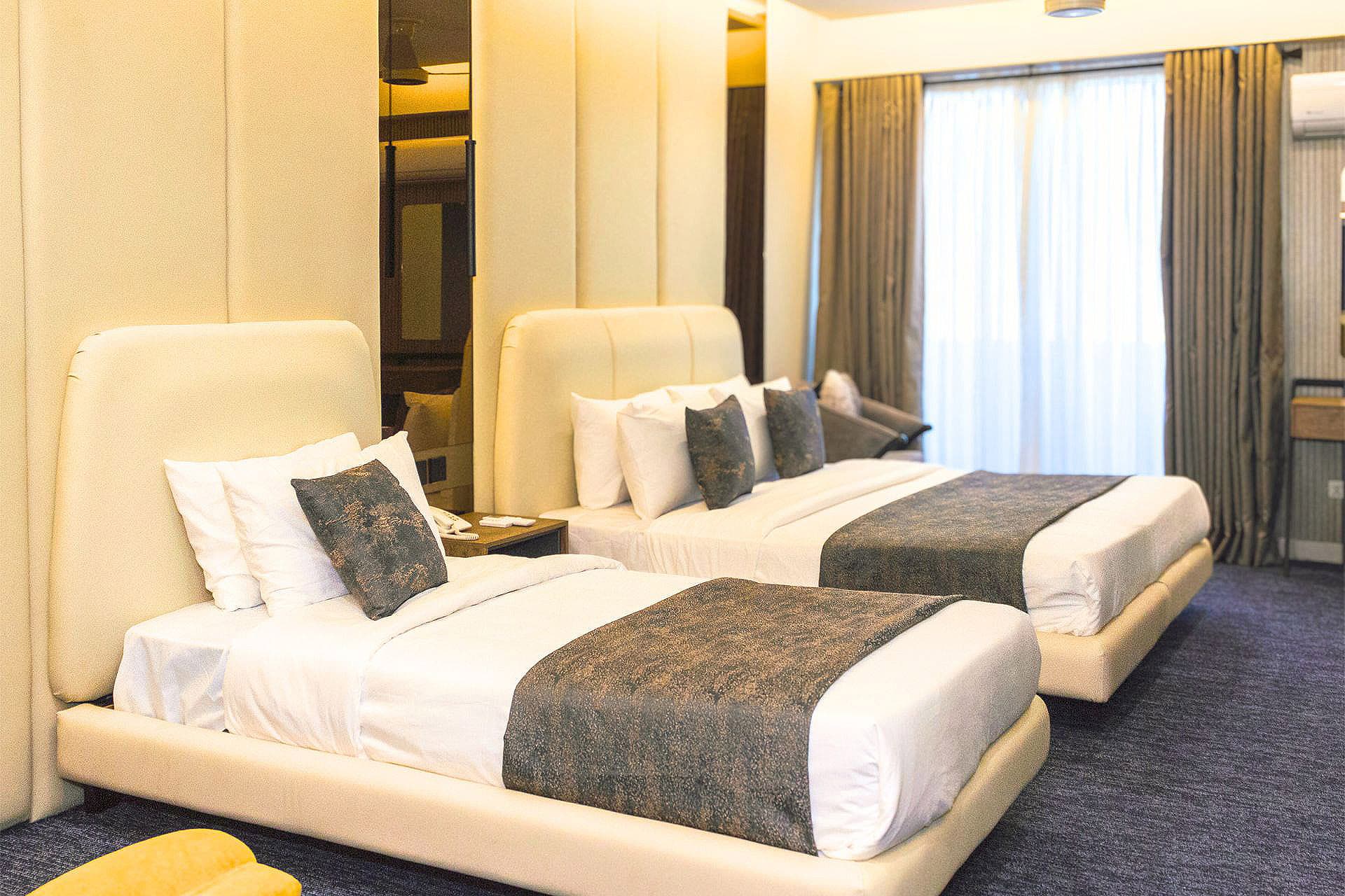 Family Room full view with king bed and single bed, curtains, window, study table, AC, mirrors, and pillows at LEORK Hotels Rawalpindi Islamabad