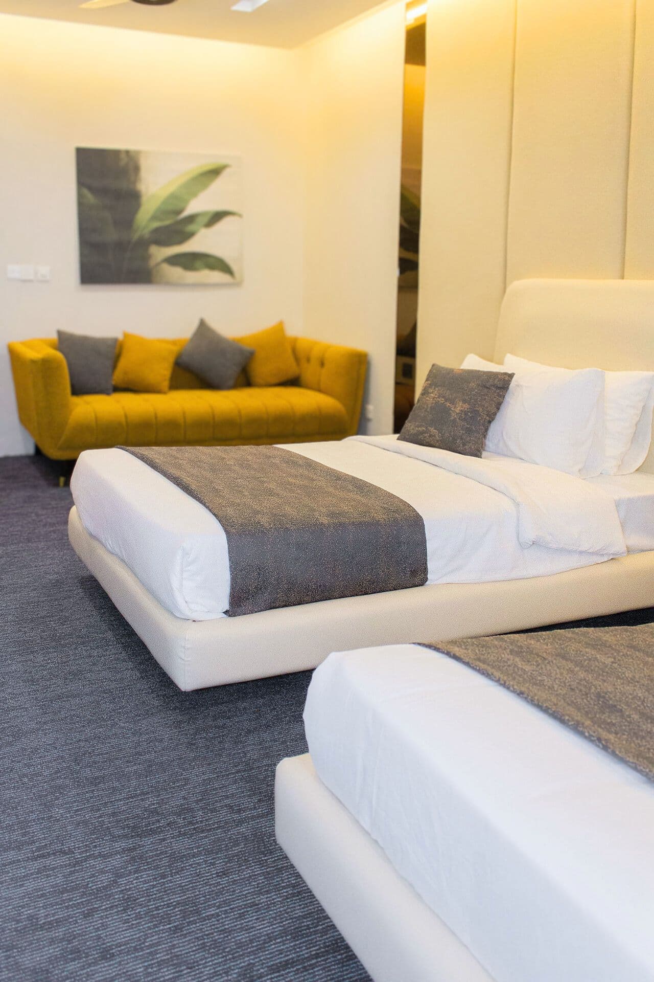 Family Room mobile view with extra bedding, three-seater sofa, AC, painting, mirror, phone, remotes, side tables, and pillows at LEORK Hotels Rawalpindi Islamabad