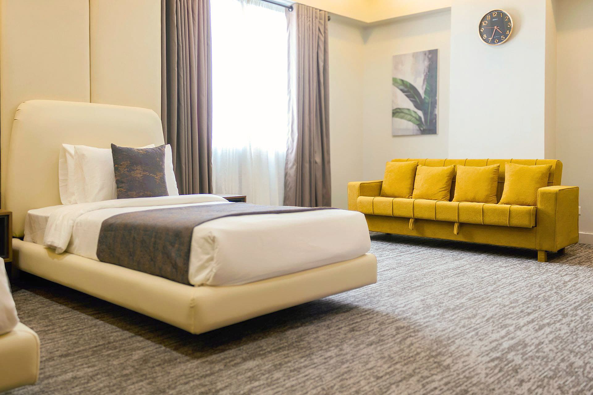 Twin Room full view with sofa cum bed, curtains, window, painting, carpet, and pillows at LEORK Hotels Rawalpindi Islamabad